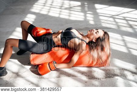 Pretty And Attractive Sportswoman Posing In A Light Studio Lying On The Floor With A Large Orange Pu