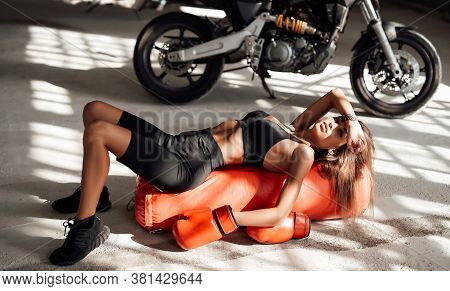 Muscular And Attractive Sportswoman Posing In A Light Studio Lying On The Floor With A Large Orange 