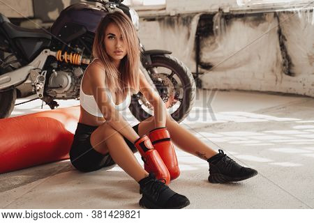 Beautiful And Attractive Looking Sportswoman Posing In A Light Studio Sitting On The Floor With A La