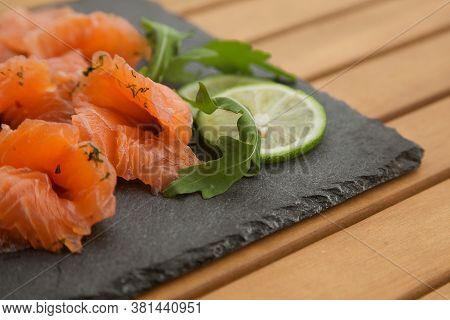 Slices Of Lightly Salted Salmon On A Black Plate Close Up On A Wooden Table.