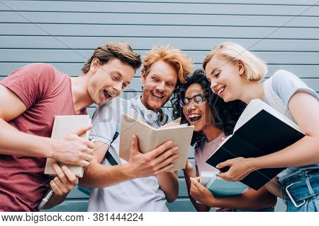 Low Angle View Of Excited Multicultural Students Reading Book On Urban Street