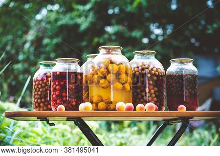 Jars With Kompot On Table. Sealed Glass Jars With Kompot Placed On Table Near Flowers And Fruits On 