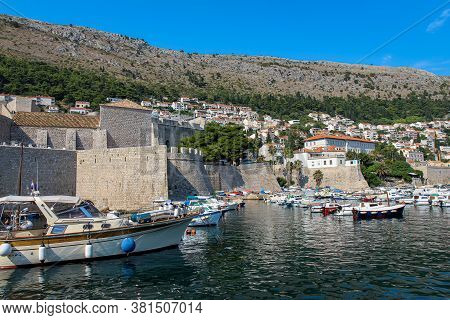 Boats Moored In Dubrovnik Harbour By The City Walls Of The Old Town And Srd Mountain, Croatia
