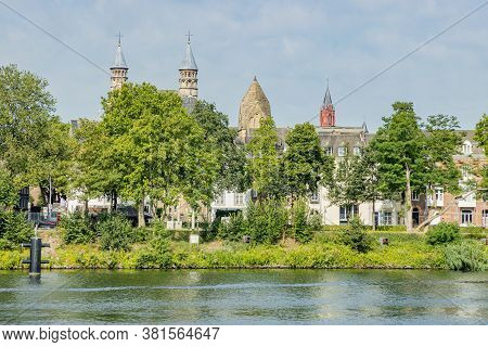 Green Trees On The Banks Of The Maas River, A Street, Houses, The Towers Of The Basilica Of Our Lady