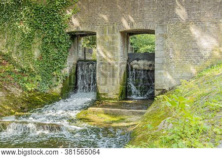 Two Floodgates On A Brick Wall Of A Weir On The Jeker River In Maastricht City Park, Sunny Summer Da
