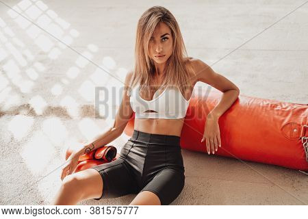 Pretty And Attractive Sportswoman Posing In A Light Studio Sitting On The Floor With A Large Orange 