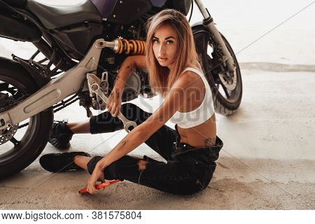 Sexy Young Girl With Wrenches Posing In A Light Photo Studio With A Sports Motorcycle