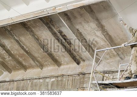Painter Worker Paints The Surface Of An Old Reinforced Concrete Slab Coating With White Paint
