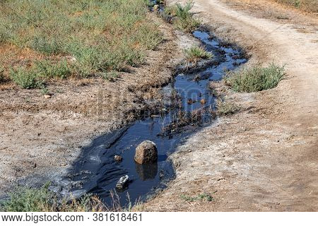 Spilled Streams Of Liquid Crude Oil Flow Down Drainage Ditch Into Public Body Of Water. Environmenta