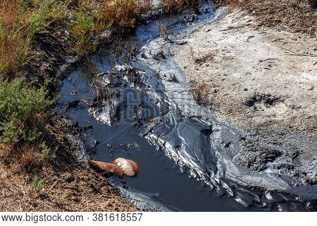 Spilled Streams Of Liquid Crude Oil Flow Down Drainage Ditch Into Public Body Of Water. Environmenta