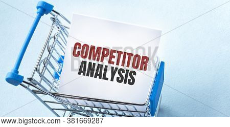 Shopping Cart And Text Competitor Analysis On White Paper Note List. Shopping List Concept On Blue B
