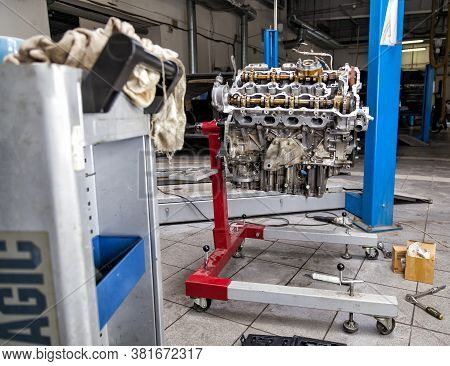 An Eight-cylinder Iron Engine Removed From A Car Near A Blue Lift In Service On A Red Stand Against 