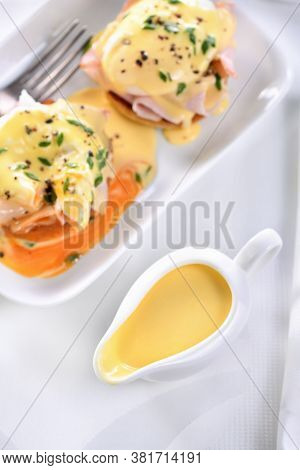 Hollandaise Butter Sauce In A Gravy Boat For Breakfast Served With Eggs Benedict- Fried English Bun,