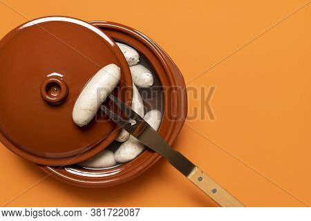 Boiled Weisswurst, German White Sausage Cooked In A Ceramic Pot, On Orange Background. Top View Of B