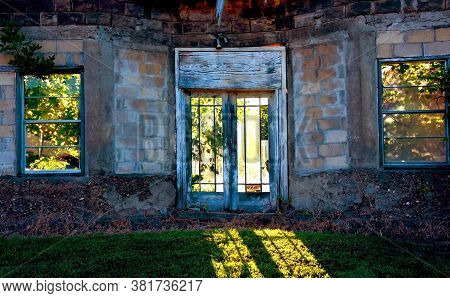 Light Streams Through An Abandoned Building's Glass Doors, With Broken Panes, And Strams Onto The Ou