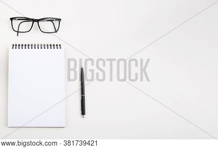White Notepad With Black Pen And Glasses On Light Table,