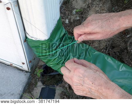 A Man Is Installing An Automatic Recoiling Extender Over The Downspout That Rolls Out When It's Rain