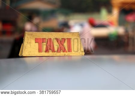 Taxi Light Sign Or Cab Sign In Drab Yellow Color With Red Text On The Car Roof At The Street Blurred