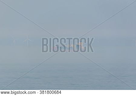 Kiel, Germany - May 11, 2011: A Container Ship Is Passing A Large Offshore Windpark During Fog Close