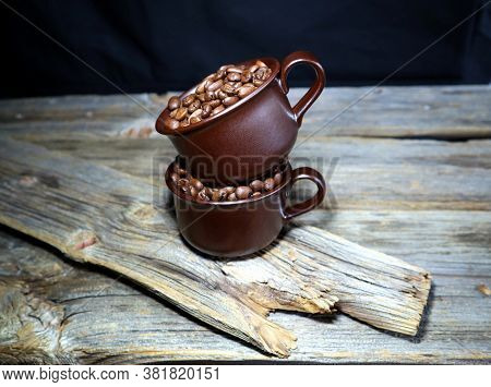 2 Brown Ceramic Coffee Cups With Coffeebeans On A Old Wooden Board