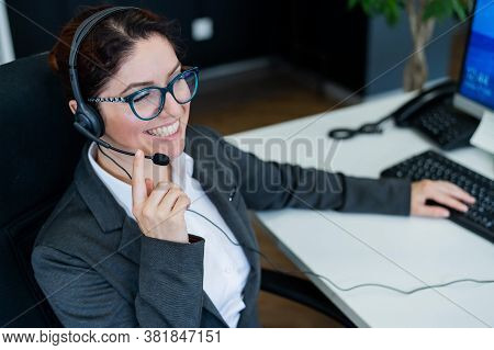 A Friendly Female Call Center Operator At The Desk. The Woman In The Headset Answers The Customers C
