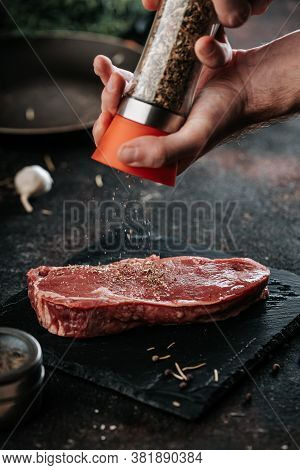 Sirloin Steak Preparation, Seasoning With Pepper And Salt. Chef Preparing Fresh Meat On Dark Marble 