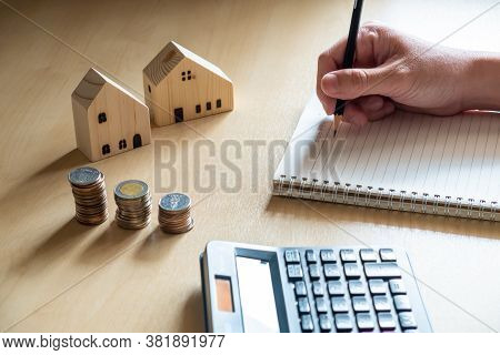 Selective Focus At Men Hand Take Note On Paper Notebook. With Blurred Calculator And House Mock Up O