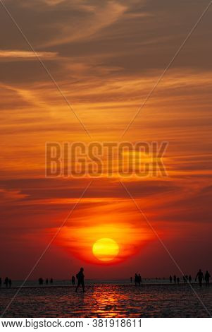 Silhouettes Of People On The Mudflap Beach Against The Sunset Sky.