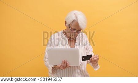 Confused Senior Woman Trying To Insert Credit Card In The Laptop. Online Shopping . High Quality Pho