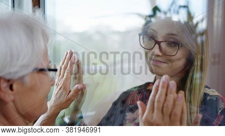 Young Lady In Quarantine Speaking With Her Grandmother Through The Glass Window. Protecting Vulnerab