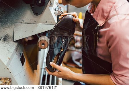 Woman cobbler working on machine in her shoemaker workshop adjusting the settings