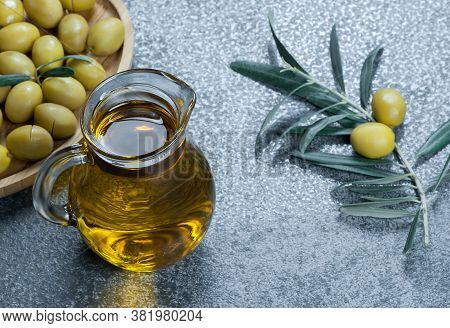 Glass Bottle Of Olive Oil And Olive Tree Branch, Raw Turkish Green Olive Seeds And Leaves On  Rustic