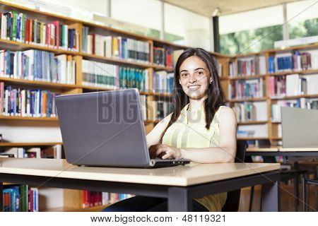 Souriante étudiante travailler avec ordinateur portable dans une bibliothèque de l'école secondaire