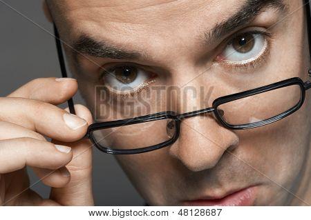 Zbliżenie portret biznesmena z ręką na okulary, co twarz szarym tle