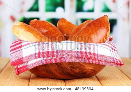 Empanadillas al horno frescos, en un recipiente de madera, en la mesa de madera, sobre fondo brillante