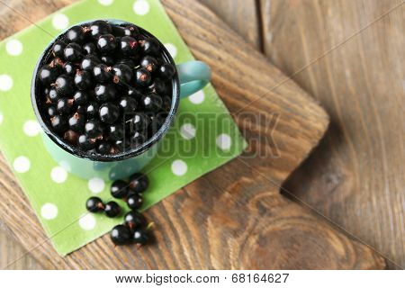 Ripe blackcurrants in mug on board, on wooden background.