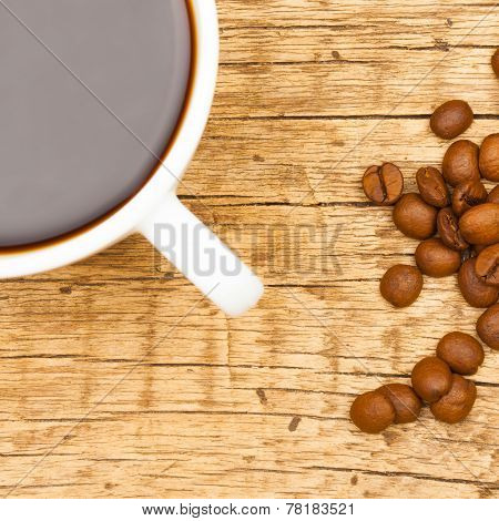 Close Up Of White Ceramic Coffee Cup With Roasted Coffee Beans On Wooden Table - View From Top