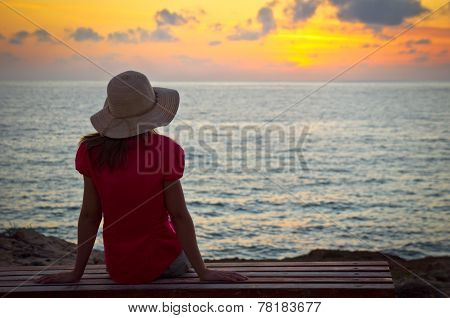 Young woman in hat sitting and looking at sunset