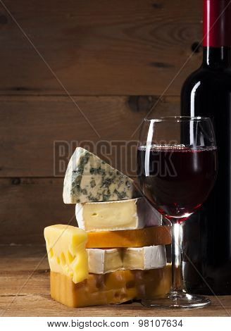 Red wine with various types of cheese on wooden background