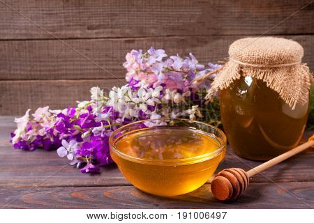 Jar of honey with wildflowers on a dark wooden background.