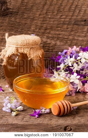 Jar of honey with wildflowers on old wooden background.