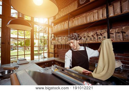 Cheerful young woman rolling a knead through pasta machine and smiling. Making pasta. Making pasta in restaurant. Woman rolling dough in cafe