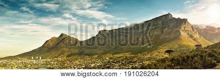 Breathtaking landscape panorama of table mountain, in cape town, south africa, with dramatic clouds and warm sunlight casting a shadow from the mountain over the city.