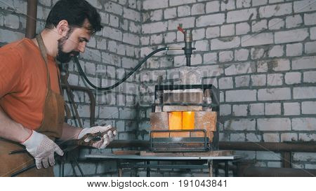 Blacksmith with a beard, sets in the grip the red-hot blanks of the future knife