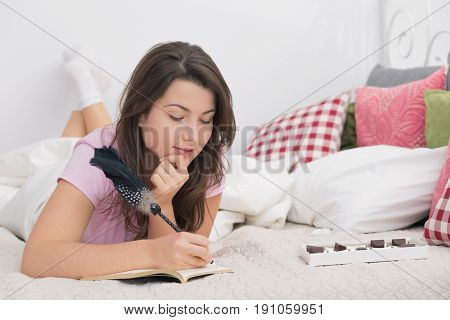 Young woman in pajamas is spending evening in bed with diary