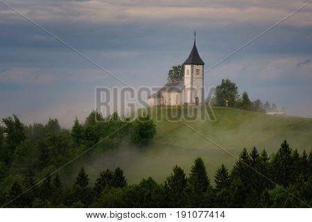 Jamnik church on a hillside in the spring, foggy weather at sunset in Slovenia, Europe. Mountain landscape shortly after spring rain. Slovenian Alps.
