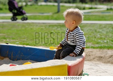 Portrait of toddler child outdoors. One year old baby boy playing with sand at playground sandbox
