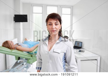 Mature female doctor posing confidently at the hospital female patient lying on gynecological chair on the background medicine healthcare feminine health gynecology professionalism trust.