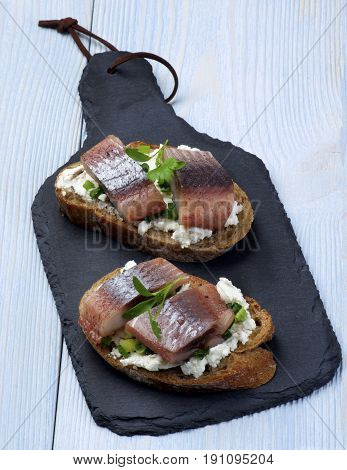 Delicious Sandwiches with Marinated Herring Cream Cheese and Chives on Slices of Brown Bread closeup on Slate Board on Wooden background