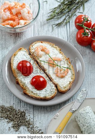 Two open sandwiches with tomatoes and shrimps on a white wooden table